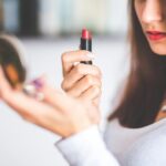 Close-up of woman applying red lipstick while holding a compact mirror.