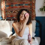 Woman with curly hair removes makeup using a cotton pad in a cozy, stylish bedroom.