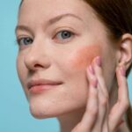 Woman applying blush on her face, highlighting healthy skin and beauty in a studio setting.