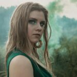 Portrait of a young woman with glitter makeup outdoors, surrounded by green foliage.