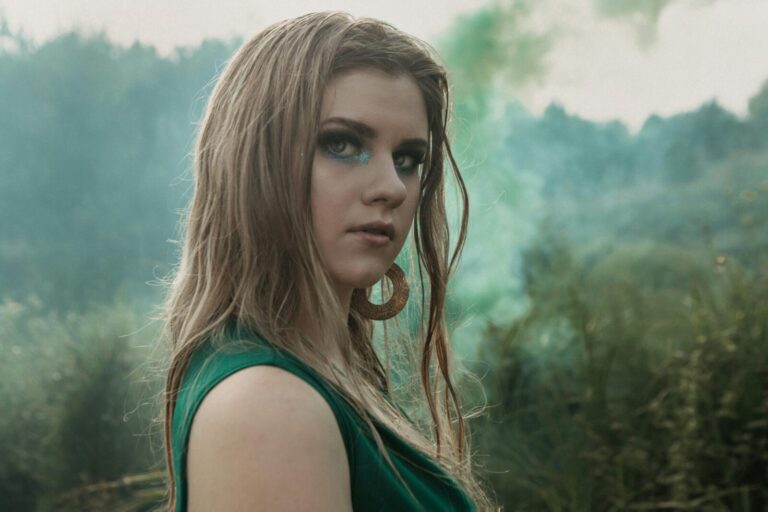 Portrait of a young woman with glitter makeup outdoors, surrounded by green foliage.